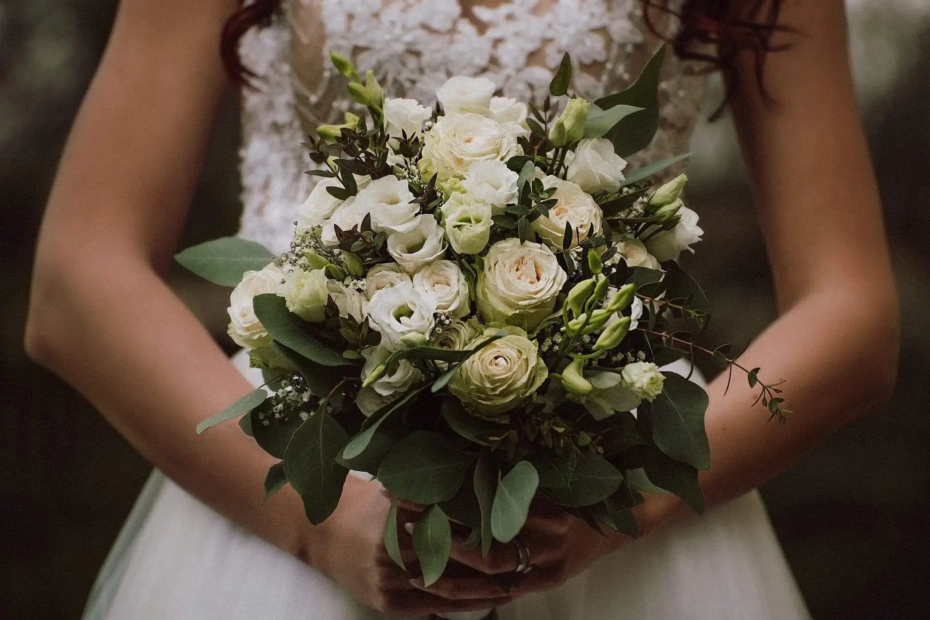 Die Braut hält einen Brautstrauß aus weißen Rosen und Grün
