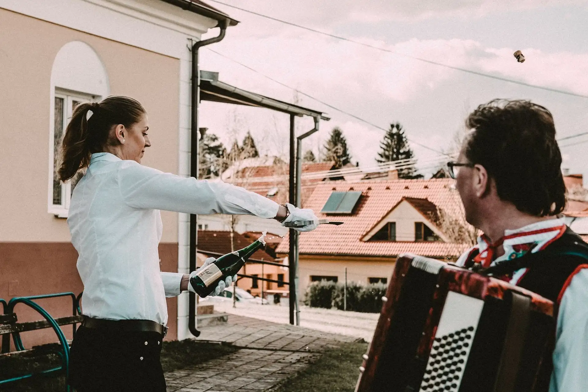 Der Service öffnet auf der Terrasse eine Flasche, daneben spielt ein Akkordeonspieler