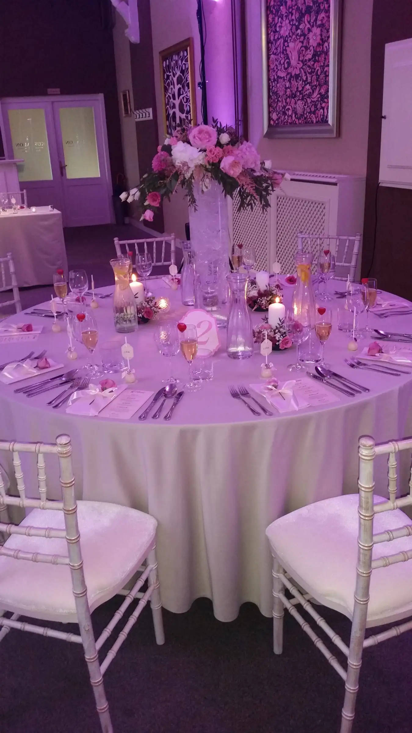 Runder Tisch mit Chiavari-Stühlen und Blumen in violettem Licht