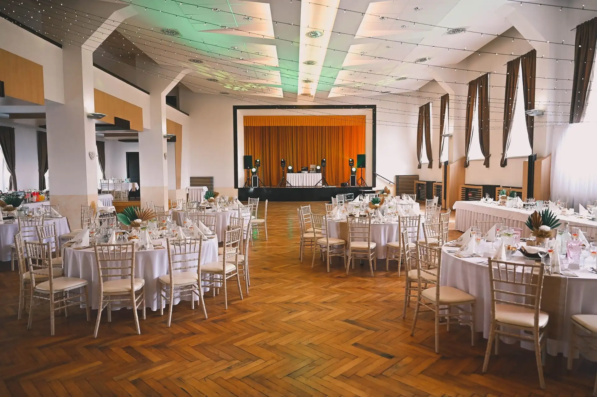 Eingedeckter Saal mit runden Tischen, Chiavari-Stühlen und einer Bühne für die Band