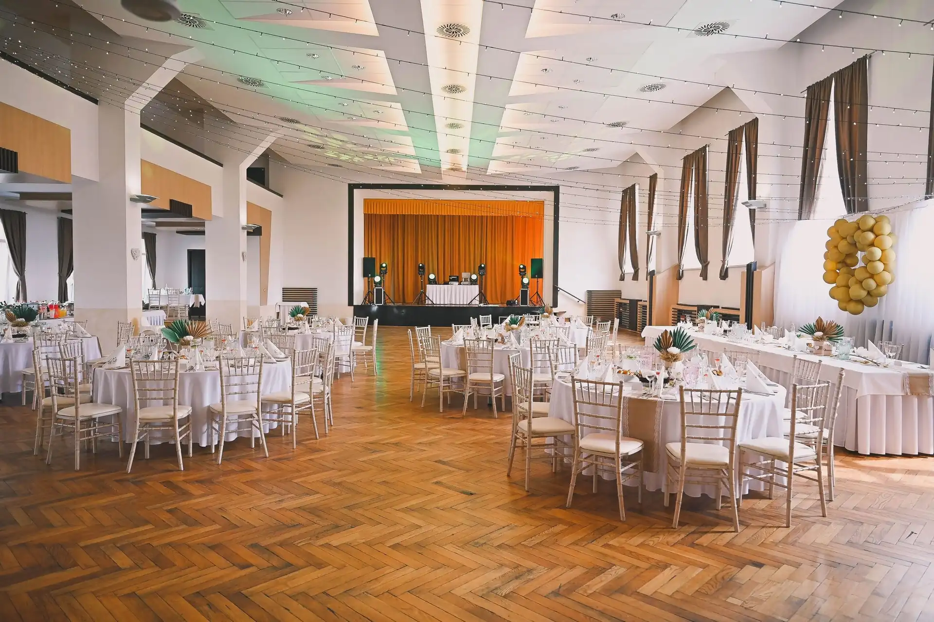 Saal mit runden Tischen, Chiavari-Stühlen und goldenen Ballons an der Bühne