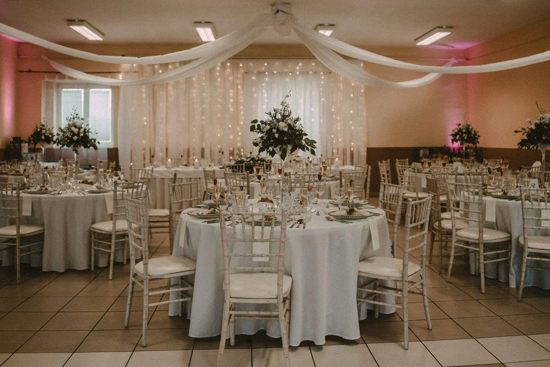 Hochzeitssaal mit runden Tischen, Chiavari-Stühlen LimeWash und einer Lichterwand aus Lichterketten